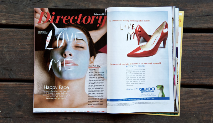 A centre spread of a womens' magazine on a wooden bench. On the left hand page is a woman with a face pack on, the words'Love Me' have been cut out of her face. On the right hand page is a pair of red high heeled court shoes.