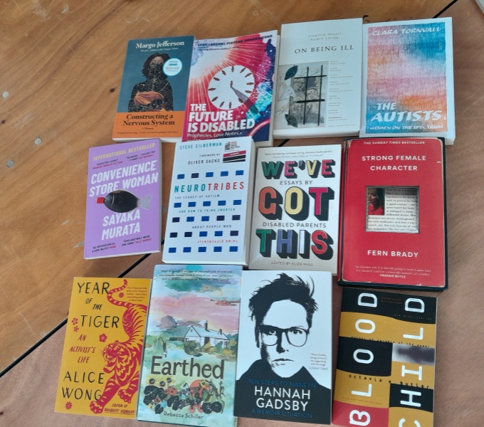 A selection of 12 books with the theme of disability laid out on a wooden table.