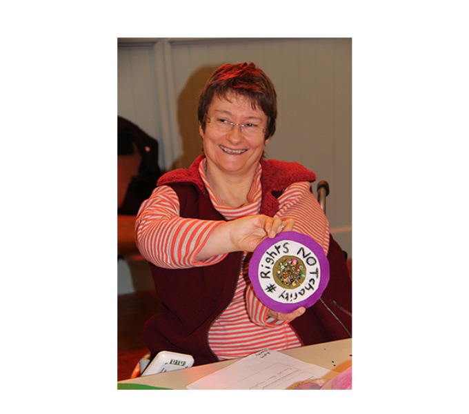 Disabled Artist Tanya Raabe-Webber smiles as she holds a purple and white rosette up to the camera