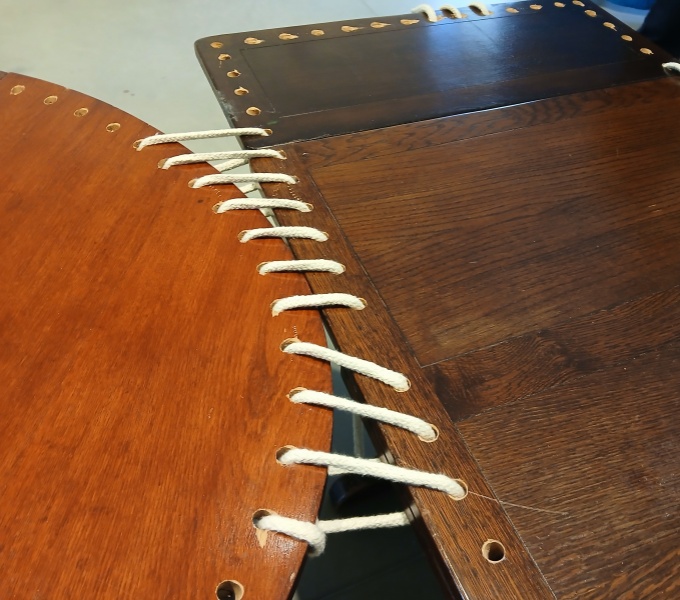 Old wooden tables with holes around the outside. Where  the tables join rope is laced through the holes joining them together.