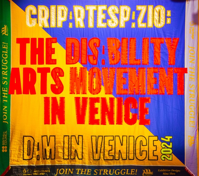 Crip arts banner in gold, red, purple colours. With slogan emblazoned across the centre: Yje Disability Arts Movement in Venice.