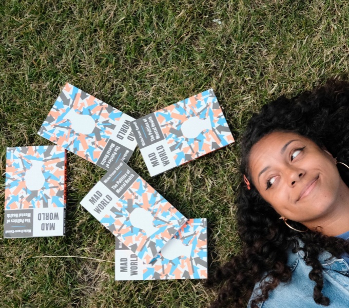 Micha lies on grass with fie copies of her book, 'Mad World' scattered around her head. 