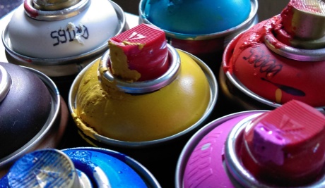 Assorted used spray cans in pink, yellow, blue , red and white grouped together with paint dripping from the nozzles.